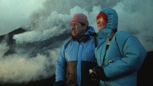 Man and woman in stocking caps and winter jackets stand before a gray, billowing cloud.